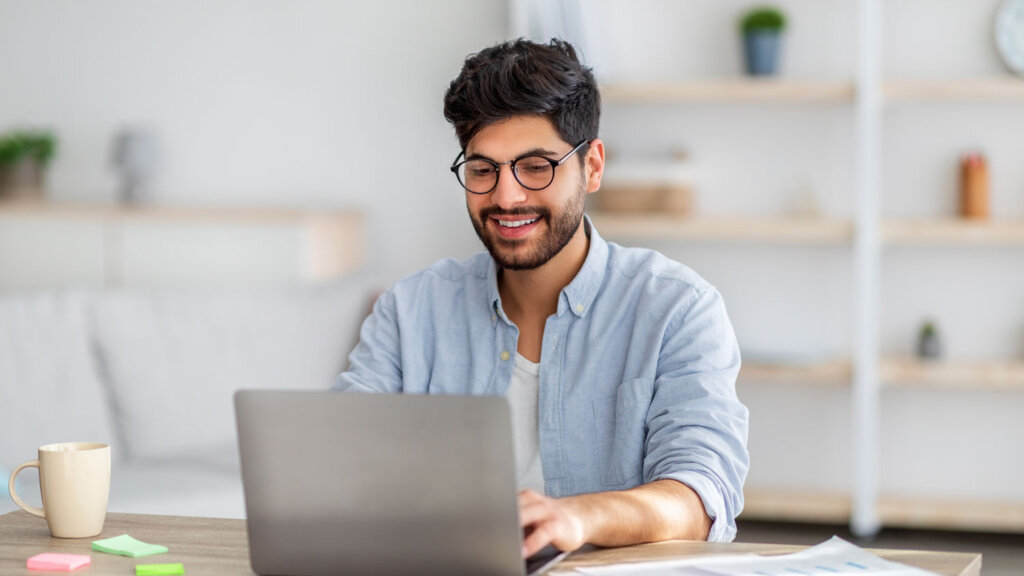 A luxury travel agent researching the best luxury host travel agencies on his laptop at a desk with a coffee cup and sticky notes next to him