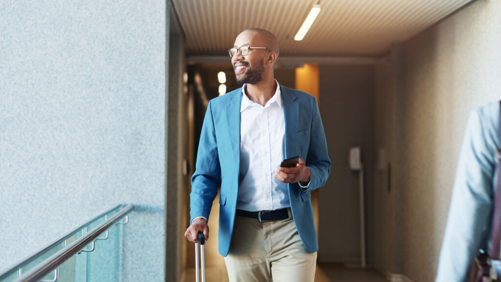 A new luxury travel advisor on his first trip walking through an airport with his suitcase and a smile on his face
